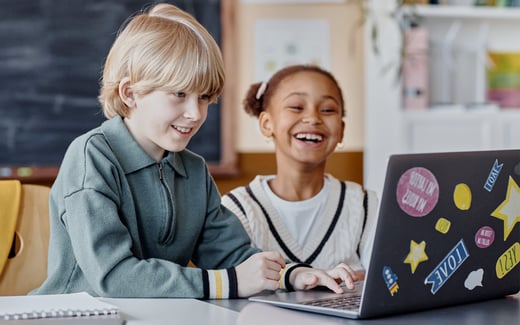 Two smiling kids at a laptop